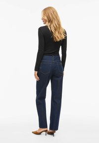 Mørkeblå denimjeans med rett ben, med baklommer og høy midje. Kombinert med en svart langermet topp og brune hæler.