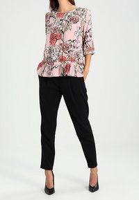 Floral peplum blouse in light pink with red and black flowers; paired with black tapered pants and pointed black heels.
