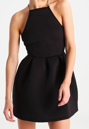 Vestido negro de tirantes halter hecho de tela ligera. Presenta un corpiño ajustado y una falda acampanada con pliegues, textura suave y tirantes ajustables.