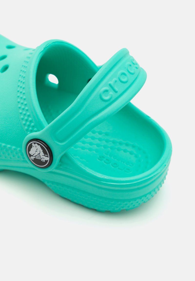 Zuecos turquesa Crocs con correa en el talón, diseño perforado y suela texturizada. Presenta un logo circular en la correa. Fabricado con material ligero.