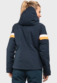 Marineblaue, wasserdichte Jacke mit verstellbarer Kapuze, ausgestattet mit weißen und orangefarbenen Streifen an den Ärmeln sowie einem eleganten, strukturierten Stoffdesign.