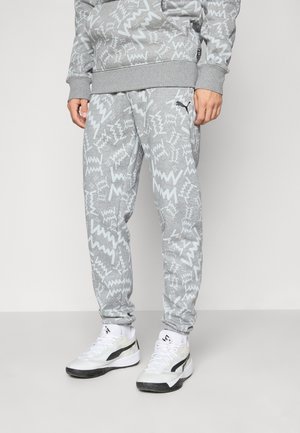 Man wearing gray patterned sweatpants and matching sweatshirt with white and black athletic shoes standing on a plain background.