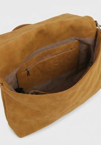 Intérieur d’un sac à main en daim beige montrant une doublure en tissu et une poche intérieure zippée avec le logo embossé "HVISK".