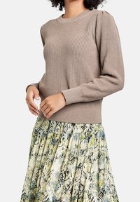Brun strikket sweater med ribbet tekstur og puffede ærmer, parret med en farverig plisseret nederdel med slangeskinmønster.