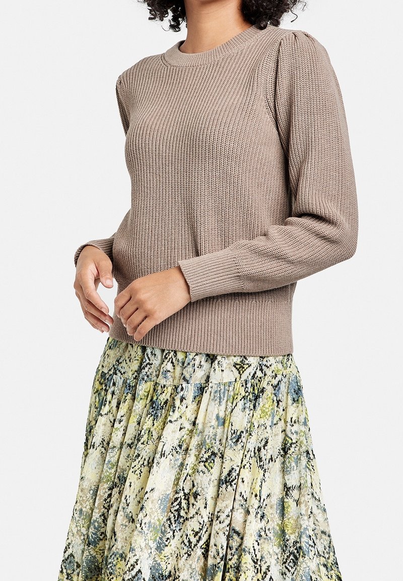 Brun strikket sweater med ribbet tekstur og puffede ærmer, parret med en farverig plisseret nederdel med slangeskinmønster.