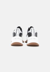Αντρινευόμενα αθλητικά παπούτσια σε ασπρόμαυρο με υφή στην επάνω επιφάνεια, αντίθετες μαύρες λεπτομέρειες στη φτέρνα, λευκή μεσαία σόλα και καφέ λαστιχένια εξωτερική σόλα.
