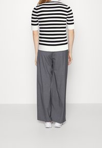 Maglione a maniche corte a righe bianche e nere abbinato a pantaloni grigi con vestibilità ampia, completato da sneakers bianche.