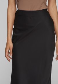 Svart, figursydd kjol med en slät textur. Hög midja, utan synliga detaljer eller mönster, som mjukt faller ned till fållen.