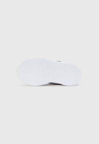 White textured sole of a sneaker against a plain gray background, showing grip pattern and curved shape.
