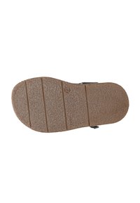 Hnědá guma podrážka sandálů s texturovaným povrchem, obsahující horizontální drážky a malý detail s logem. Plochý design pro stabilitu.