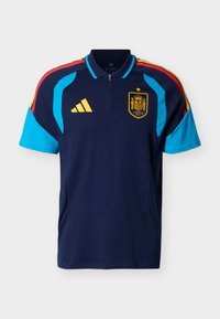 Tamsiai mėlynas Ispanijos futbolo marškinėlis su šviesiai mėlynomis rankovėmis, raudonais ir geltonais peties dryžiais, Adidas logotipu ir Ispanijos nacionalinės komandos emblemą su žvaigžde.