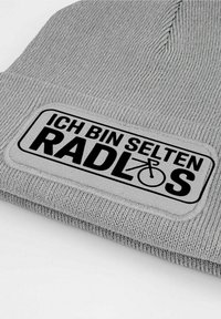 Gray knitted beanie with a textured surface and a rectangular patch displaying "ICH BIN SELTEN RADLOS" in bold black letters.