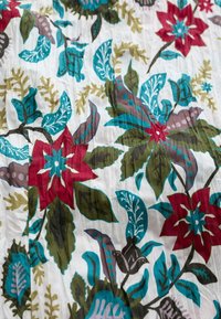 Blomstret stof med røde, blå og grønne blomster og blade på en hvid baggrund. Blød tekstur med en krøllet overflade.