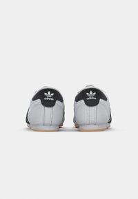 Obuv Adidas s šedým syntetickým svrškem, černými koženými doplňky a gumovou podrážkou, s bílým logem na patě.