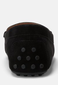 Svart mocka loafers med platt häl. Har en texturerad gummisula med runda nitar för bra grepp. Slät innervadd är synlig.