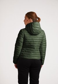 Grøn puffjakke med hætte, med et quiltet design, glat tekstur og vandrette striber. Sorte bukser under.