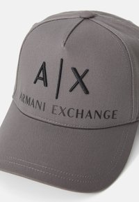 Grå baseball caps laget av stoff, med hevet svart tekst "A|X" og "ARMANI EXCHANGE" på forsiden, med en glatt tekstur.