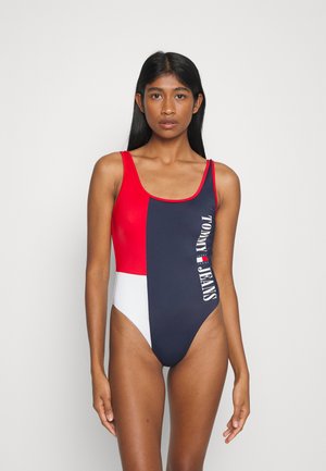 Bañador bloqueado en rojo, azul marino y blanco con escote redondo. Presenta el logo "TOMMY JEANS" impreso verticalmente en un lado. Textura suave.