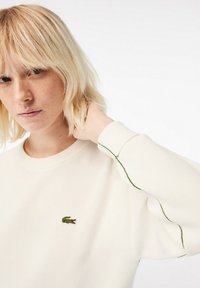 Crème sweatshirt met een gestructureerde afwerking, voorzien van groene accenten langs de mouwen en een klein geborduurd krokodillenlogo op de borst.