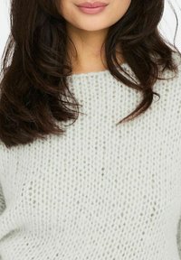 Pull en maille gris clair avec un tricot lâche et ouvert, encolure large et texture douce. Dispose de manches longues et d'une coupe décontractée.