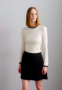 Langsleeve, aansluitend wit topje met een zwarte ronde halslijn en zwarte afwerking, gecombineerd met een zwarte A-lijn rok. Gladde stof, minimalistisch ontwerp.