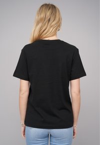 T-shirt en coton noir avec des manches courtes et un col rond, présenté de dos. Texture lisse avec une coupe décontractée.