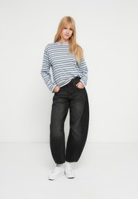 Μπλούζα με ρίγες και μακριά μανίκια σε ανοιχτό μπλε, ναυτικό και λευκό χρώμα· συνδυασμένη με μαύρα τζιν ψηλόμεσα, άνετης εφαρμογής· λευκά αθλητικά παπούτσια.