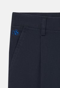 Navy blue trousers featuring a smooth texture, front pockets, and a small blue embroidered logo on the waistband.