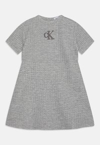 Grå bomullsklänning med korta ärmar, rund halsringning, texturerat tyg och en kontrasterande brun broderad "CK"-logotyp på bröstet.