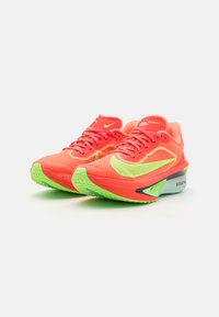 Rote und gelbe Nike Zoom Fly Laufschuhe mit einem Mesh-Obermaterial, strukturierten Oberflächen und einer grünen Gummisohle mit auffälligen Markenakzenten.