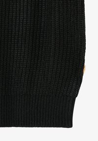 Schwarzer Strickstoff mit einem gerippten Muster und einem kleinen beigen Etikett am rechten Seitenrand.