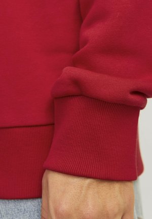 Red sweatshirt with ribbed cuffs. Smooth texture, fitted design around the wrist. Visible stitching details and a straight hemline.