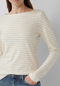 Lightweight long-sleeve top in cream with thin beige horizontal stripes. Features a boat neck and fitted sleeves. Soft, textured fabric.