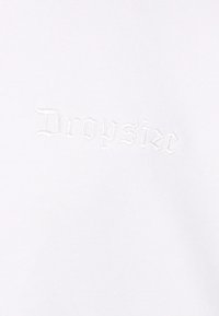 Hvid T-shirt med "Dropsize" broderet i lys tråd, med et minimalistisk design og en blød, glat tekstur.