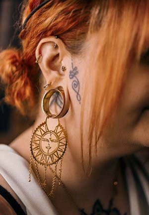 Goldene Creolen-Ohrringe mit einem kreisförmigen Sonnendesign und darunter hängenden Ketten. Der Ohrring weist ausgeklügelte Ausschnitte und Details auf.