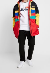 Röd, gul, grön och svart vadderad jacka med dragkedja, med färgblockerad design och logotyp. I kombination med vit sweatshirt och svarta byxor.