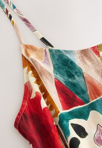 Gros plan d'une robe à bretelles spaghetti à motifs avec des formes abstraites en rouge, sarcelle, brun, violet et beige sur fond clair.