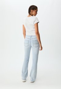 Svetlo siva majica s kratkimi rokavi v kombinaciji s svetlo modrimi flared kavbojkami, ki imajo dva zadnja žepa in rahlo povišan pas.