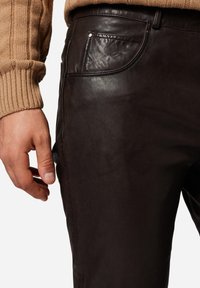Brune læderbukser med en glat tekstur, der har en sidelomme og diskret syninger, båret med en ribbet beige sweater.