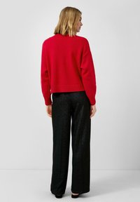 Roter, kurz geschnittener Pullover mit geripptem Saum, kombiniert mit schwarzen, weit geschnittenen Hosen aus glänzendem Material. Das Outfit wird von hinten betrachtet.