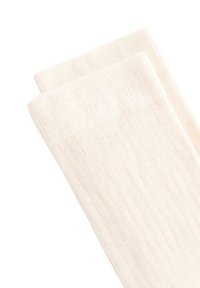 Dva presavijena čarapa od rebrastog pletiva boje kreme složena jedna na drugu na bijeloj pozadini.