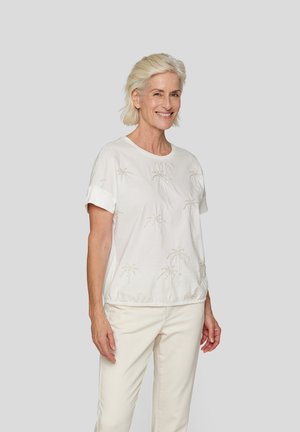 White short-sleeve blouse with embroidered palm tree design, elastic hem, and soft texture. Paired with light cream pants.