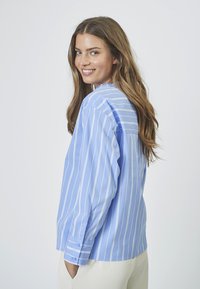 Blue striped button-up shirt with long sleeves, featuring a relaxed fit and a slight sheen, pocket detail, and cuffed sleeves.