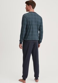 Blauwe en groene geruite blouse met lange mouwen en een ronde hals, gecombineerd met donker marineblauwe pantalons, beide gemaakt van zachte stof.