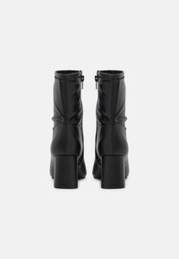Bottines en cuir noir avec un talon bloc, présentant des détails froncés et une fermeture éclair à l'arrière. Texture lisse sur l'ensemble.