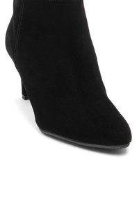 Juodas zomšinis kulkšninis botas su smailiu pirštu ir mažu sudėtiniu kulnu. Savybės - toniniai siūlai ir sklandi viršutinė tekstūra.