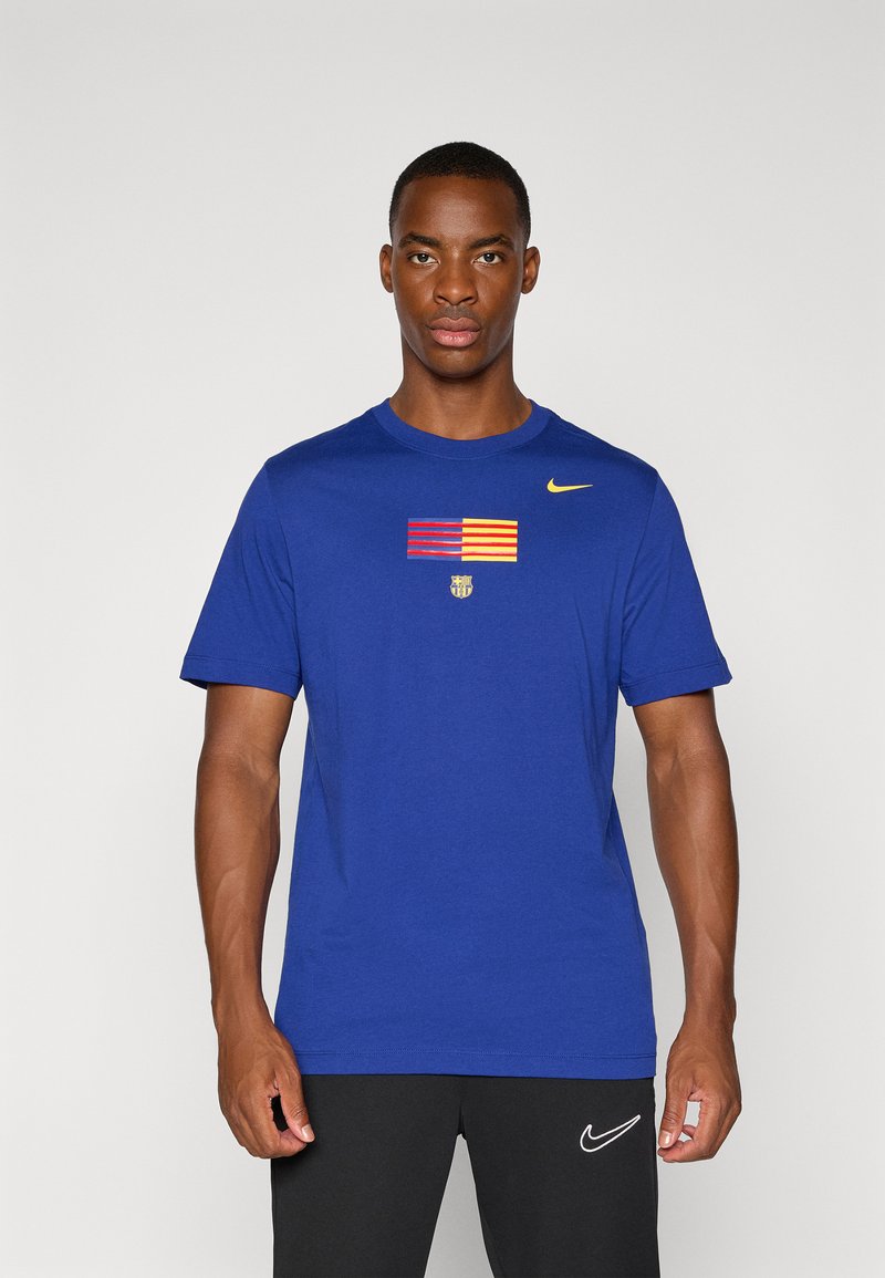 Blå bomulds T-shirt med et horisontalt stribet mønster i rød og gul, et centralt emblem og et lille Nike-logo på skulderen.