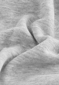 Tissu gris clair avec une texture douce et lisse. Le matériau présente un motif tricoté subtil et des plis délicats, affichant une apparence décontractée.