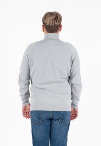 Maglione grigio con colletto alto, polsini e orlo a coste. Presenta una texture liscia ed è progettato con maniche raglan per facilitare i movimenti.