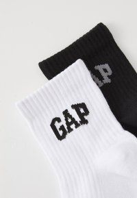 Baumwollmischsocken in Weiß und Schwarz, mit geripptem Muster und dem "GAP"-Logo in kontrastierenden Farben auf jeder Socke.